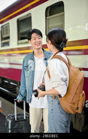 Ein glückliches und reizendes junges asiatisches Touristenpaar spricht gerne, bevor es am Bahnhof in den Zug steigt. Stockfoto