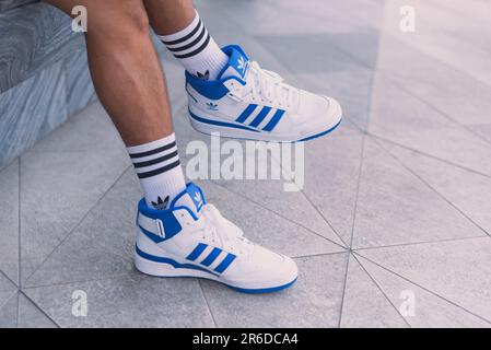 Adidas Forum Mid weiße und blaue Sneaker auf Männerfüßen auf der Straße, eine Nahaufnahme am 20. Mai 2023 in Bangkok, Thailand. Stockfoto