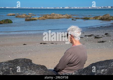 Eine Seniorin am Strand im Sommer mit weißen Haaren und Sonnenbrille Stockfoto