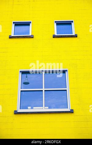 Fenster an der gelben Wand. Zwei Fenster mit weißen Rahmen und einer gelben Wand. Außenansicht eines Hauses mit Fenstern. Wunderschöne, farbenfrohe Hausfassade. N Stockfoto