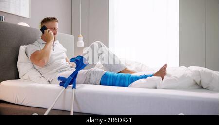 Glücklich, junger Mann mit gebrochenem Bein Sitzen auf einem Sofa Gespräch am Handy Stockfoto