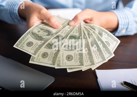 Eine junge Geschäftsfrau, die Bargeld zählte, hundert Dollar Scheine, Finanzdokumente überprüfte, am Tisch saß, Papiere und Steuern Stockfoto