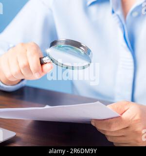 Professionelle Geschäftsfrau, die Hand hält und mit einer Lupe nach Finanzdokumenten sucht, die auf dem Schreibtisch im Büro liegen, Geschäftsfrau, die sich Daten ansieht Stockfoto