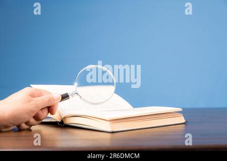 Offenes Buch mit Lupe auf Holzschreibtisch in Informationsbibliothek der Schule oder Universität, Konzept für Bildung, Lesen, Lernen, Kopierbereich und b Stockfoto