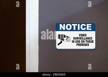 Blau-weißes Hinweisschild an der Seite einer offenen Tür mit der Aufschrift „Hinweis, Videoüberwachung in diesen Räumlichkeiten in Gebrauch“. Stockfoto