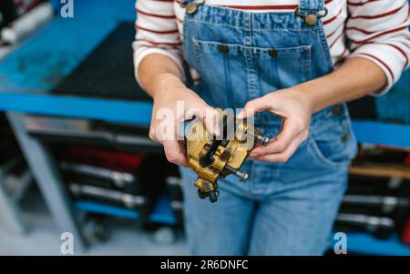 Eine Mechanikerin, die das Bremssattelsystem vor der Werkbank überprüft Stockfoto