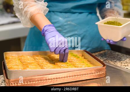 Nahaufnahme von Händen bei der Zubereitung traditioneller türkischer Baklava-Süßigkeiten mit Pistazien in einer Bäckerei in Istanbul. Herstellung von Baklava Stockfoto