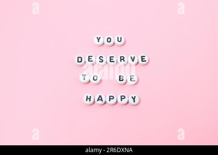 Draufsicht der Zitate „You deserve to be happy“ mit Perlen auf pinkfarbenem Hintergrund. Motivation und Erfolgskonzept Draufsicht von „Du verdienst es, glücklich zu sein“ Stockfoto