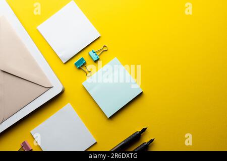 Flache Anordnung von schwarzen Stiften, Umschlägen, Büroklammern und Notizen mit Kopierbereich auf gelbem Hintergrund. Schulmaterial, Schreiben, Malen, Zeichnen, lear Stockfoto