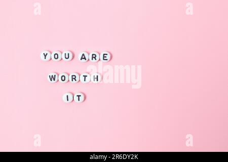 Draufsicht der Zitate „You're worth it“ aus Perlen auf pastellfarbenem Hintergrund. Motivation und Erfolgskonzept Stockfoto