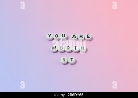 Draufsicht der Zitate „You're worth it“ aus Perlen auf pastellfarbenem Hintergrund. Motivation und Erfolgskonzept Stockfoto