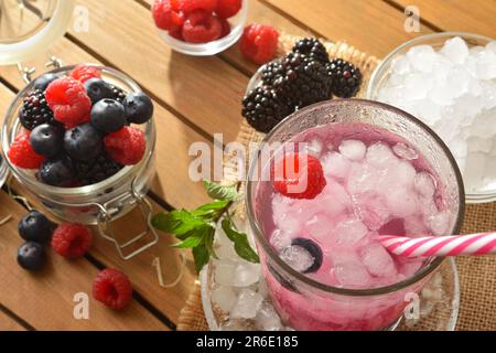 Fruchtgetränk mit Brombeeren, Himbeeren und Blaubeeren auf einem Holztisch mit Behältern voller Obst und Eis. Draufsicht. Horizontale Zusammensetzung. Stockfoto