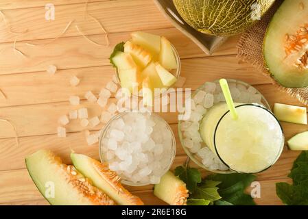 Details des Eismelonengetränks in einem Glas auf einem Holztisch mit Obst und zerstoßenem Eis. Draufsicht. Horizontale Zusammensetzung. Stockfoto
