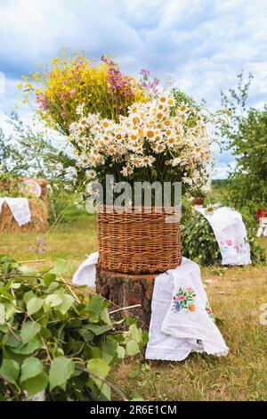 Ein Korb voller wilder Blumen auf einem Feld auf einem Baumstumpf Stockfoto