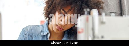 Konzentrierter afro-amerikanischer Schneidermeister zieht Skizzenbuch ein, das am Arbeitsplatz mit einer modernen Nähmaschine sitzt Stockfoto