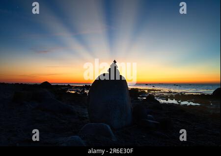 Steinpyramide an der Ostsee mit Blick auf das Meer bei Sonnenuntergang. Die Sonne scheint hinter der Steinpyramide. Steine als Silhouette. Spirituelle Sichtweise. Querformat f Stockfoto