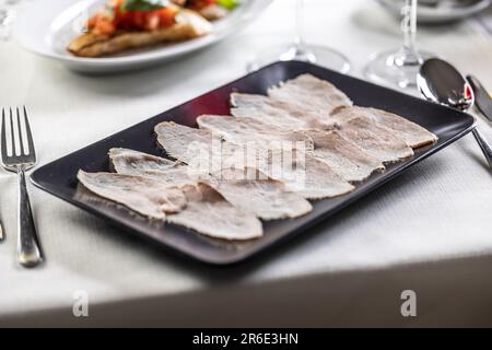 Dünn geschnittenes Kalbfleisch mit einer Thunfischsalsa, serviert auf einem schwarzen rechteckigen Teller. Stockfoto