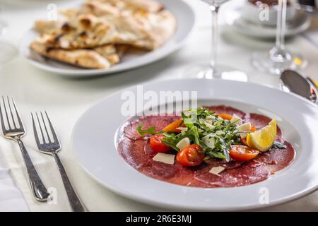 Typische italienische Vorspeise, Carpaccio aus Kalb oder Rindfleisch, dünn geschnitten und auf einem Teller mit Salat serviert. Stockfoto