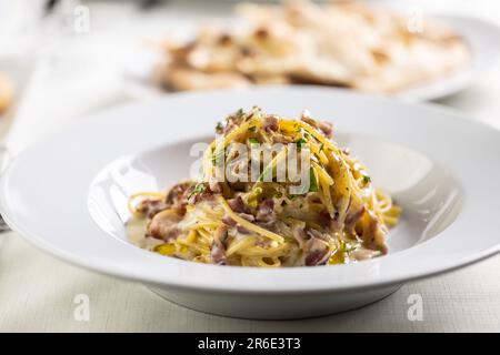 Spaghetti Carbonara mit gebratenem Speckwürfeln, gelber Sauce aus Eiern und mit grünem Salat. Stockfoto