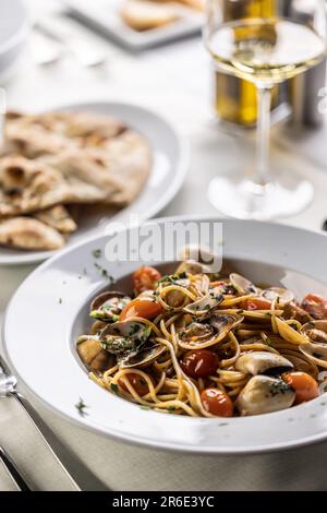 Traditionelle italienische Spaghetti alle vongole e pomodorini, serviert mit Fladenbrot und Weißwein. Stockfoto