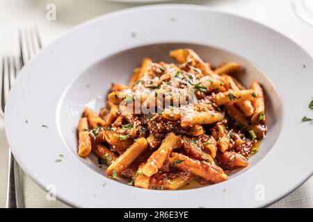 Penne alla arrabiata, typische italienische Mahlzeit, serviert auf einem schönen weißen Teller, dekoriert mit frischen Kräutern und mit geriebenem Käse. Stockfoto