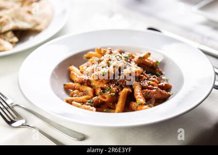 Pene alla arrabiata, italienische Pasta mit roter Sauce, serviert auf einem Tisch auf einem Teller mit frisch geriebenem Parmesan. Stockfoto