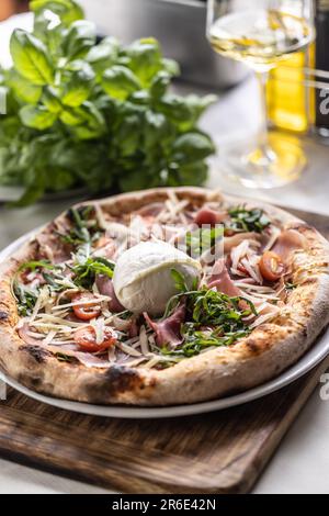 Runder Büffelmozzarella auf Schinken, Tmatos und Raketenpizza mit verkrusteten Kanten. Stockfoto
