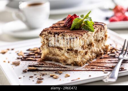 Traditioneller italienischer Tiramisu-Kuchen, serviert auf einem dekorativen Teller mit einem Espresso. Stockfoto
