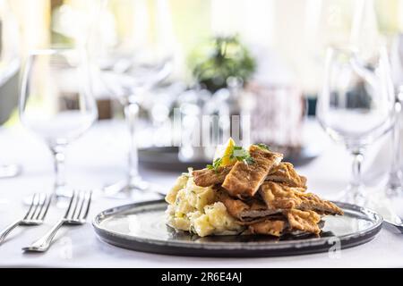 Verschiedene Präsentation eines traditionellen Schnitzels mit Kartoffelsalat, serviert auf einem schön dekorierten Restauranttisch. Stockfoto