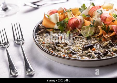 Pilzrisotto mit Wurzelgemüse neben den Gabeln auf einem weißen Tisch. Stockfoto
