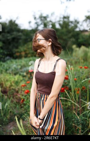 Die Frau freut sich im Sommer, allein inmitten von Blumen und grünem Gras Stockfoto