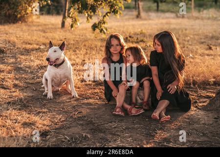 Drei Schwestern und ein Hund sitzen unter einem Baum in schwarzen Kleider in der Natur Stockfoto