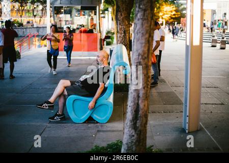 Ein Mann sitzt auf einer blauen Bank in einer Straßendokumentationsszene Stockfoto