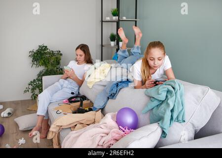 Mädchen spielen mit einem Handy. Das Zimmer ist ein Chaos. Die Kinder haben Dinge im Zimmer verstreut. Stockfoto