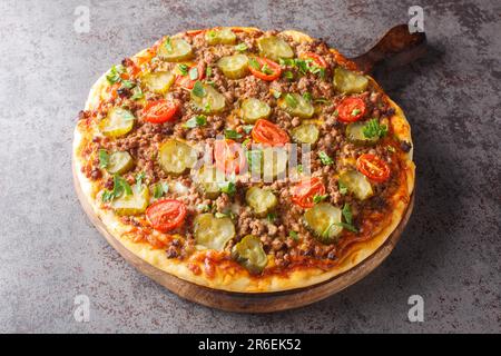Tasty Pizza wird mit einer cremigen Burgersauce, Hackfleisch, Käse und Gurken auf dem Holzbrett auf dem Tisch abgerundet. Horizontal Stockfoto