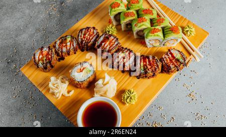 Ein hölzernes Schneidebrett mit einer Auswahl an farbenfrohen Sushi-Brötchen, darunter Thunfisch, Lachs und Gurken Stockfoto