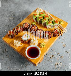 Ein Kopfschuss mit verschiedenen Sushi-Brötchen auf einem Schneidebrett, begleitet von Dippsoße Stockfoto