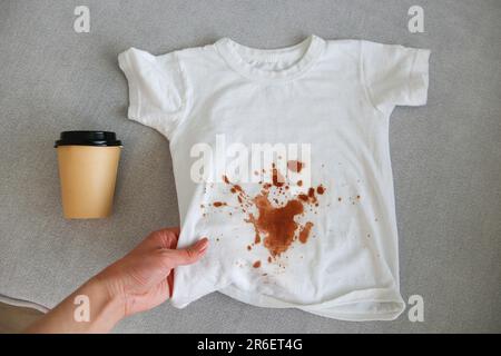 Das Kind verschüttete Kaffee auf seine Kleidung. Das Konzept eines Flecks auf einem T-Shirt. Draufsicht. Stockfoto