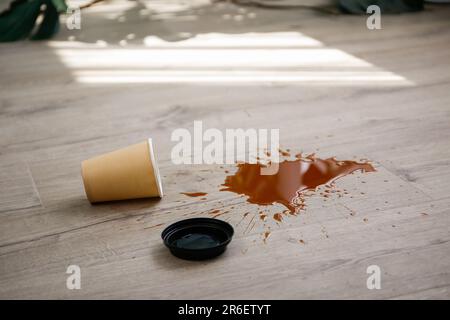 Pappbecher Kaffee fiel auf Laminat, Kaffee verschüttete auf den Boden. Stockfoto