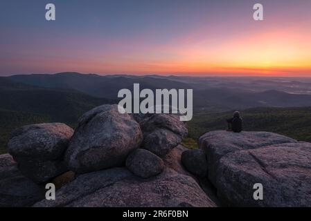 Bei Sonnenaufgang erstrahlt der Himmel in der Dämmerung mit einem Wanderer auf dem Gipfel des Old Rag Mountain im Shenandoah-Nationalpark, Virginia. Stockfoto