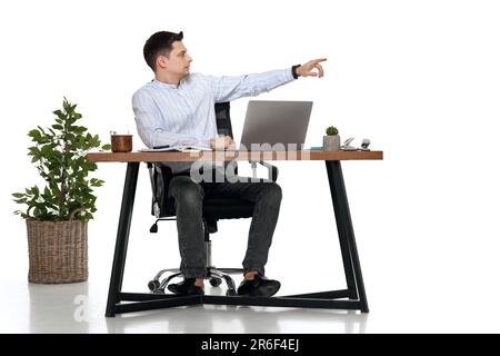 Junger Mann, der am Tisch ein Notebook benutzt und auf einen Kopierbereich zeigt Stockfoto