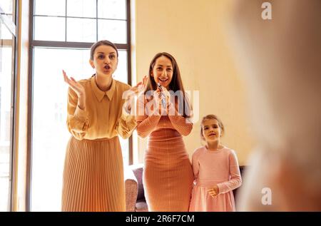 Fröhliche interrassistische Freunde spielen Rate mal, wer spielt, Pantomime-rätsel oder Scharaden zeigen, Spaß zu Hause haben. Gruppe mit verschiedenen jungen Frauen, die sich an p Stockfoto