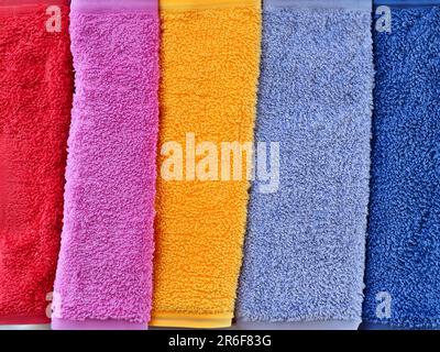 Eine Reihe bunter Handtücher, die hintereinander auf einem Regal hängen. . Stockfoto