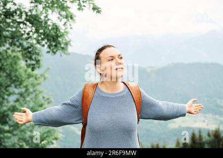 Eine Frau mittleren Alters, die in den Bergen wandert, einen Rucksack trägt, die Arme weit offen Stockfoto