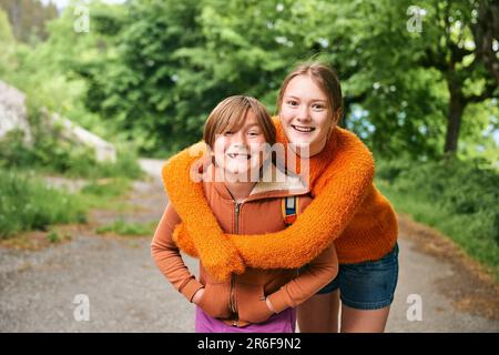 Außenporträt von zwei lustigen Kindern, die sich umarmen, Teenager-Schwester und kleiner Bruder, die draußen Zeit miteinander verbringen Stockfoto