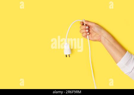 Weibliche Hand, die ein Kabel mit Stecker auf gelbem Hintergrund mit Kopierbereich hält Stockfoto