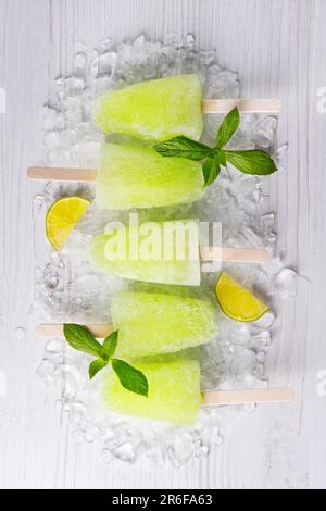 Hausgemachtes Eis am Stiel mit Limettensaft und Minze, Mojito-Fruchteis auf einem weißen Holztisch Stockfoto
