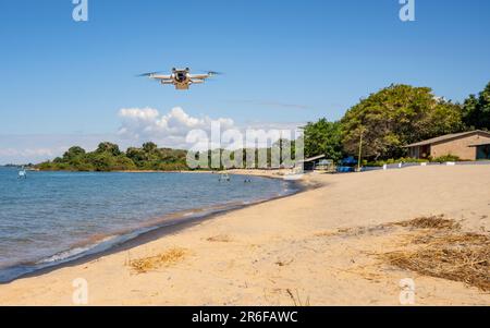 Eine DJI Mini Pro 3 Drohne schwebt am Ufer des Lake Malawi Stockfoto