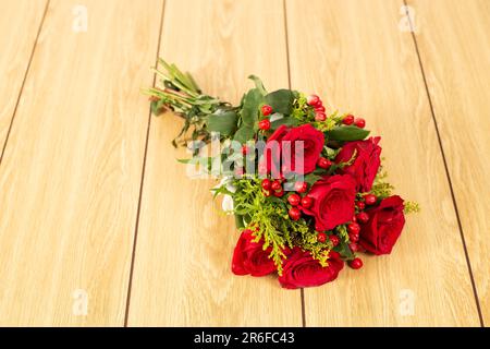Ein lebhafter Strauß frischer, roter Rosen auf einem hellbraunen Holztisch Stockfoto