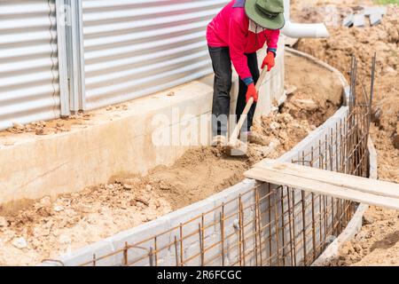 Der Arbeiter nivelliert den Boden mit einer Schaufel auf der Baustelle. Stockfoto